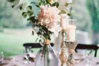 an elegant barn wedding centerpiece of metallic candleholders, a bottle with blush blooms and a mini table number