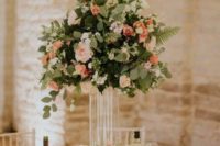 an elegant barn wedding centerpiece of peachy and blush blooms, greenery and floating candles in glasses