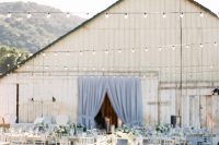 an elegant modern barn wedding reception with blue and grey linens and curtains, chic chairs and neutral florals is amazing