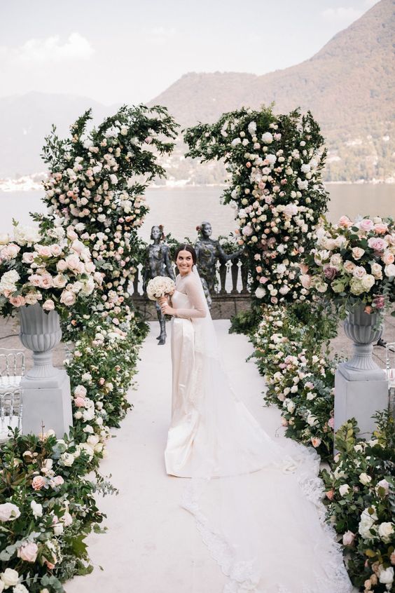 an elegant wedding ceremony space decorated with neutral and blush florals and greenery plus a lake view