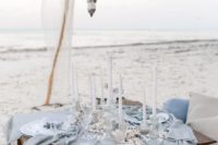 an ethereal light blue picnic setting with candle lanterns, a blue table runner, seasells and corals and white candles