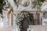 an indoor garden wedding venue with a greenery and white flower arch and matching floral arrangements lining up the aisle