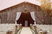 an outdoor barn wedding ceremony space wiht curtains, a wreath, some florals and tassel garlands and petals on the ground