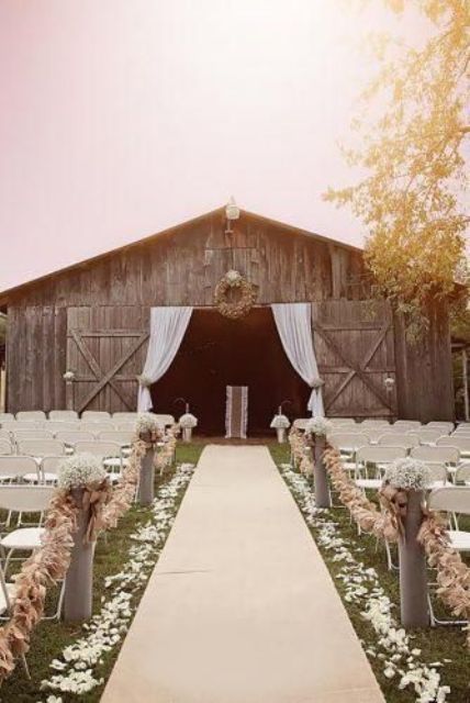 an outdoor barn wedding ceremony space wiht curtains, a wreath, some florals and tassel garlands and petals on the ground
