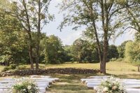 an outdoor barn wedding ceremony space with benches of hay, barrels with greeneyr and blooms and baskets
