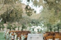 an outdoor barn wedding ceremony space with stained chairs, elegant eucalyptus and bloom arrangements, candle lanterns and string lights