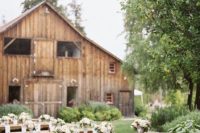 an outdoor barn wedding reception space with long tables, white linens, neutral and pink floral arrangements is a cool idea