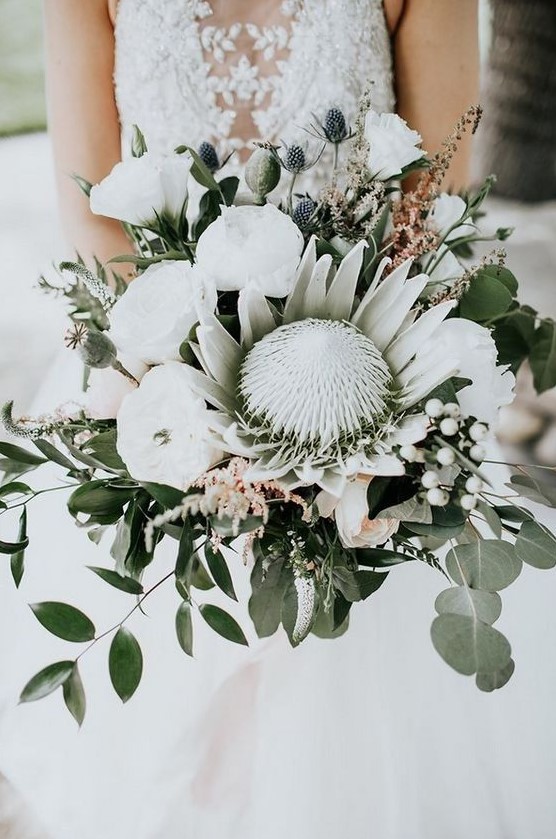 an oversized wedding bouquet of a king protea, white peonies, berries, thistles and greenery for a bold statement