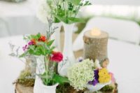 wood slices with moss, bright blooms in milk glass vases, a rustic table number and a candle on a tree stump