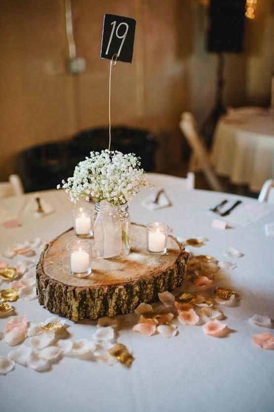 a barn wedding centerpiece of a wood slice, petals, candles and baby's breath in a jar plus a chalkboard table number