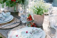 a beautiful summer wedding table setting with woven placemats, printed napkins, white and red blooms and some strawberry on the table