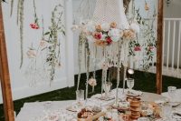 a beautiful vintage bridal shower tablescape with a tassel garland and blooms hanging down, a woven lampshade with blooms and a lovely grazing tableBridal Shower