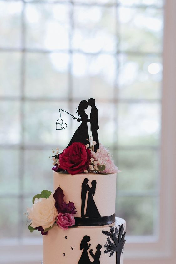 a black and white wedding cake decorated with black silhouettes and with matching cake toppers, with fresh blooms and greenery