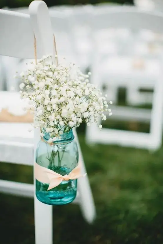 a blue mason jar with blush ribbon and baby's breath for a rustic summer aisle