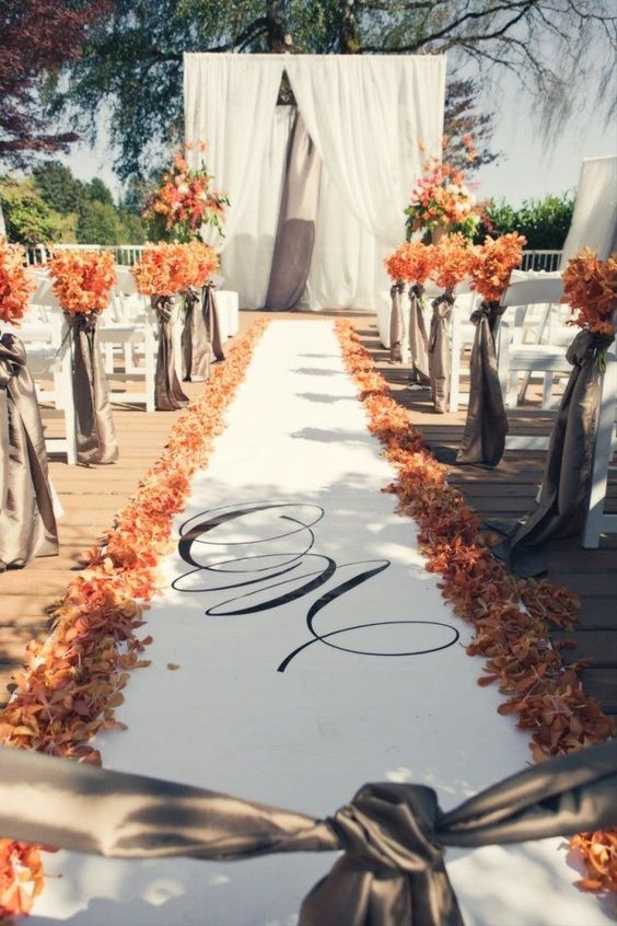 a bold fall wedding aisle with bold blooms and dried leaves on the ground and on the chairs is a very cool idea