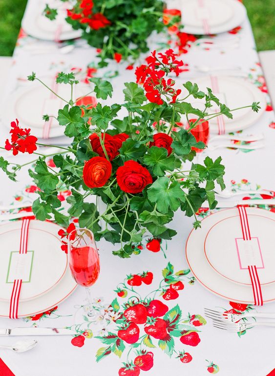 a bold summer wedding tablescape with strawberry prints, with red-rimmed plates and bold red ranuculus wedding centerpieces