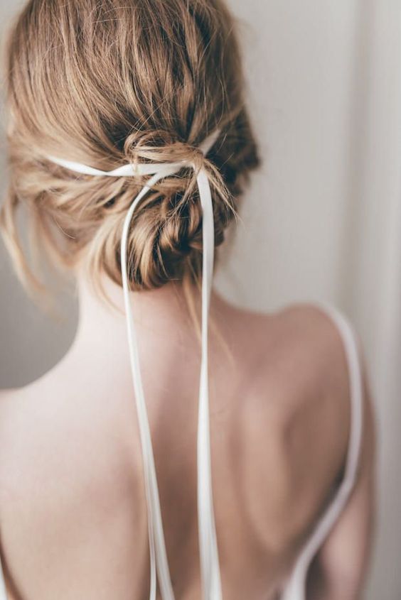 a braided low updo with a messy volume on top and a thin and delicate ribbon accenting the hairstyle