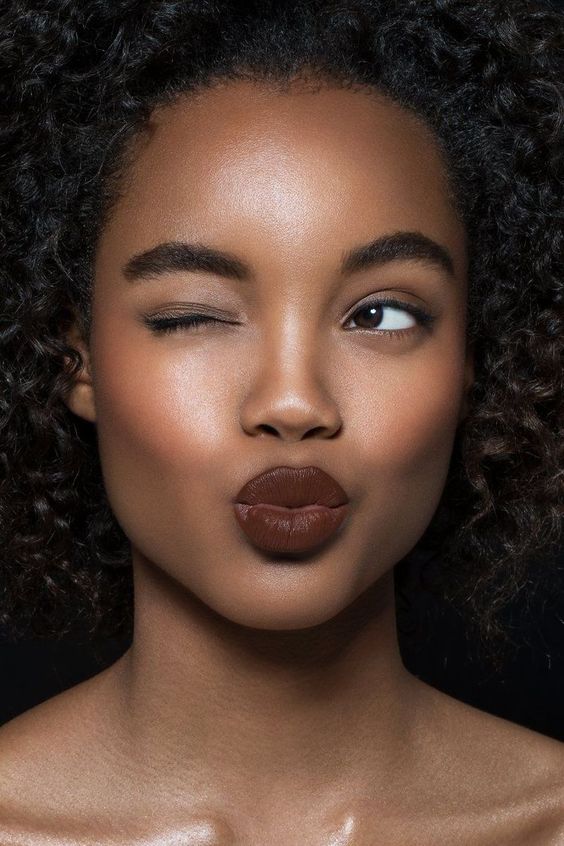 a chic makeup with perfectly matted skin, a touch of blush and highlighter, fluffy eyebrows and a dark lip
