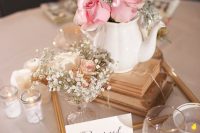 a chic vintage bridal shower centerpiece of stacked books, a teapot with pink roses, baby’s breath and candles