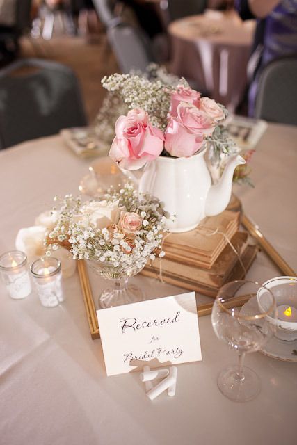 a chic vintage bridal shower centerpiece of stacked books, a teapot with pink roses, baby's breath and candles