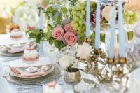 a chic vintage bridal shower tablescape with a lace tablecloth, pastel blooms and greenery, blue candles, grapes and cupcakes