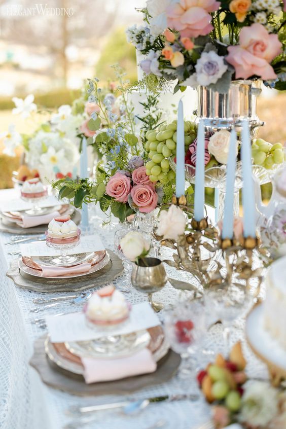 a chic vintage bridal shower tablescape with a lace tablecloth, pastel blooms and greenery, blue candles, grapes and cupcakes