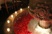 a chic vintage fountain with floating red blooms and candles on the edge is a stylish and lovely idea to go for