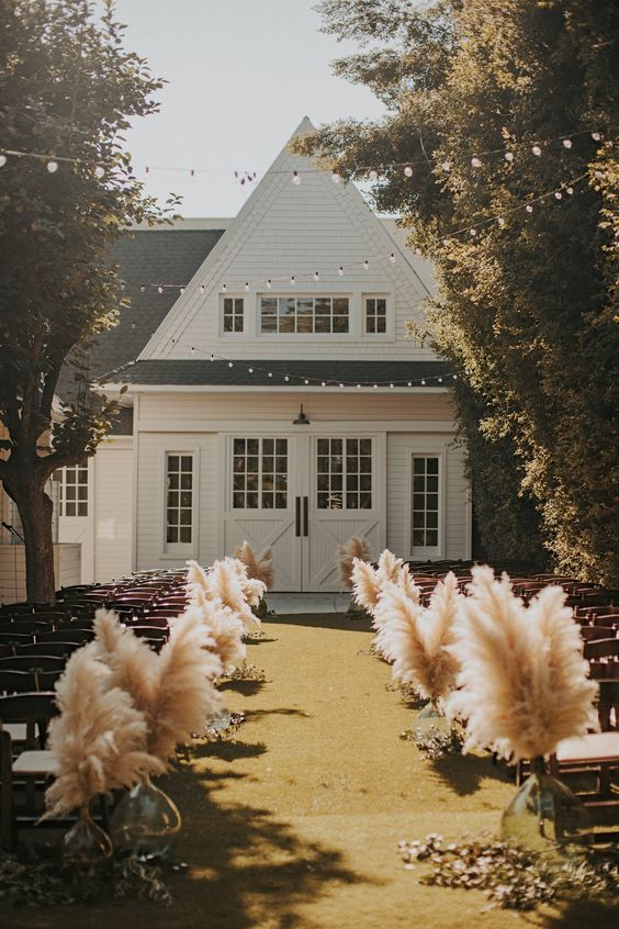 a classy boho fall wedding aisle decorated with lush pampas grass in vases and dried foliage