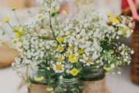 a cluster rustic wedding centerpiece of a tree slice, mason jars with twine, baby’s breath and chamomiles is a lovely idea