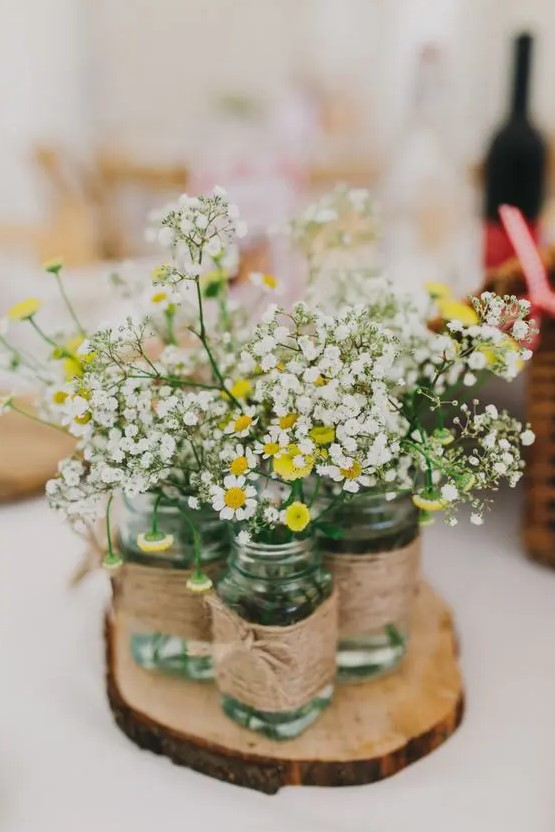 a cluster rustic wedding centerpiece of a tree slice, mason jars with twine, baby's breath and chamomiles is a lovely idea
