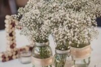 a cluster rustic wedding centerpiece of mason jars with burlap and white baby’s breath is a cool idea for a rustic wedding