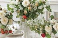 a cluster wedding centerpiece of white vases with white blooms, greenery and strawberries for a strong summer feel