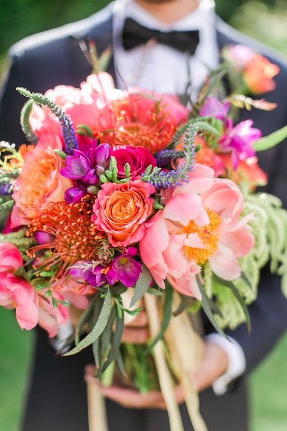 a colorful wedding bouquet of coral peonies, pink and hot pink roses, purple blooms, greenery and astilbe is a fun idea