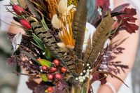 a creative boho wedding bouquet offeathers, colorful bynny tails, greenery and berries is a lovely and bold idea for a fall boho bride