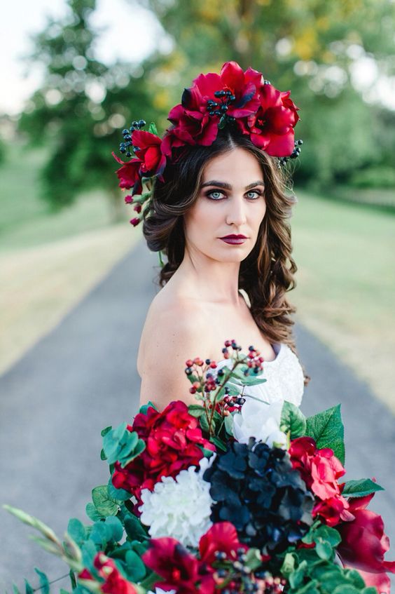 a dramatic flower crown with deep red blooms and berries and a matching bouquet is a nice idea for a Halloween or bold fall wedding