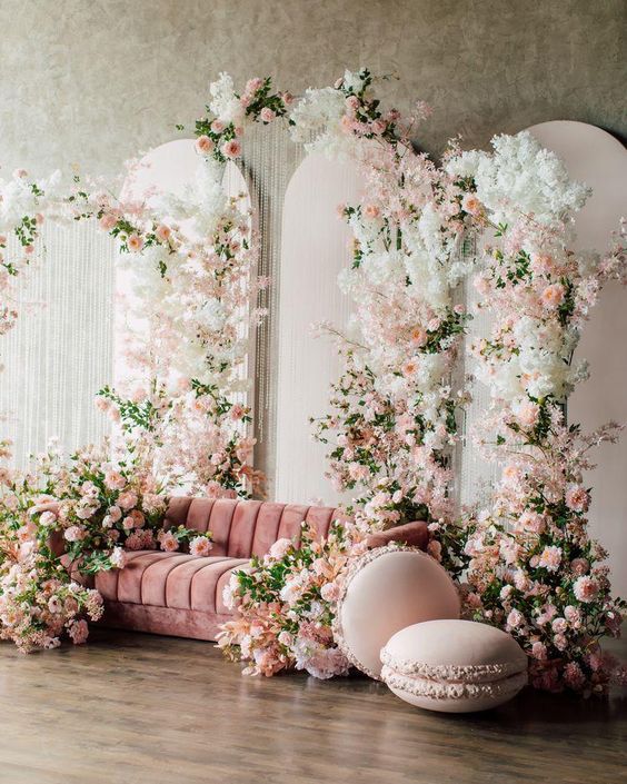a fantastic vintage bridal shower lounge with a pink sofa, neutral, blush and pink blooms and greenery and macaron poufs