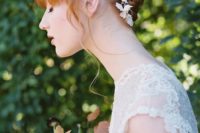 a fully braided updo with lace floral trim and bangs for a subtle and chic bridal look