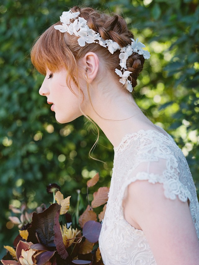 a fully braided updo with lace floral trim and bangs for a subtle and chic bridal look