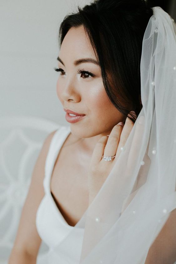 a glowy Asian wedding makeup with a shiny pink lip, extended eyelashes, coral blush and glowy skin is inspiring