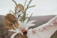 a gorgeous boho wedding bouquet of fronds, greenery, white dried greenery and butterflies is a lovely idea for a boho bride