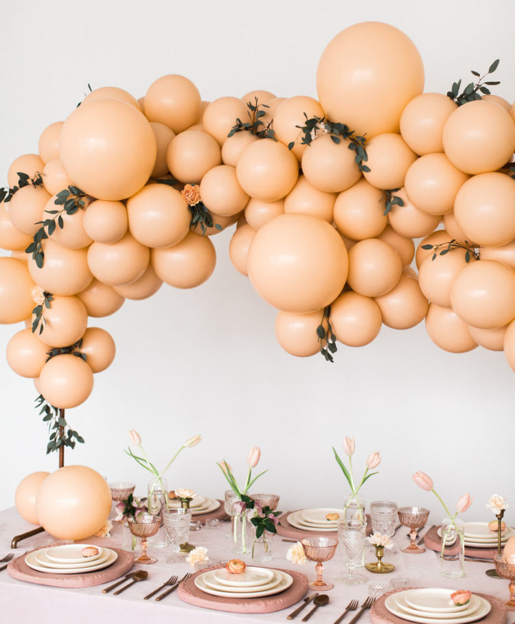a gorgeous modern bridal shower setting in blush and peachy, with a balloon overhead decoration, blush tulips and textural chargers