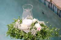 a greenery and pastel bloom arrangement with a single candle inside is a beautiful solution for wedding pool decor