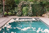 a large pool floating with white and blush blooms and a matching floral arch opposite it is a cool idea