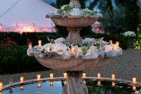 a large tiered fountain with white floating blooms and candles around it is a very cool and romantic idea to try