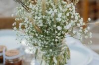 a mason jar wrapped with lace and with baby’s breath and wheat is a great rustic wedding centerpiece