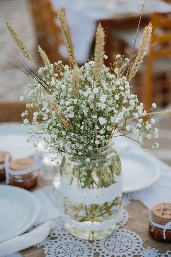 a mason jar wrapped with lace and with baby's breath and wheat is a great rustic wedding centerpiece