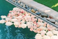 a pool lined up with pebbles and with floating neutral and pastel blooms is a refined and beautiful solution for a wedding