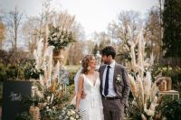 a pretty boho fall wedding aisle with neutral blooms, greeneyr and pampas grass in planters and pots is a very cool idea