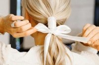 a pretty low ponytail with a texture and a white ribbon covering it and a bow is a very chic and delicate idea with a strong feminine feel