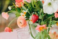 a pretty summer wedding centerpiece with orange ranunculus, pink and white poppies, strawberries and greenery is amazing